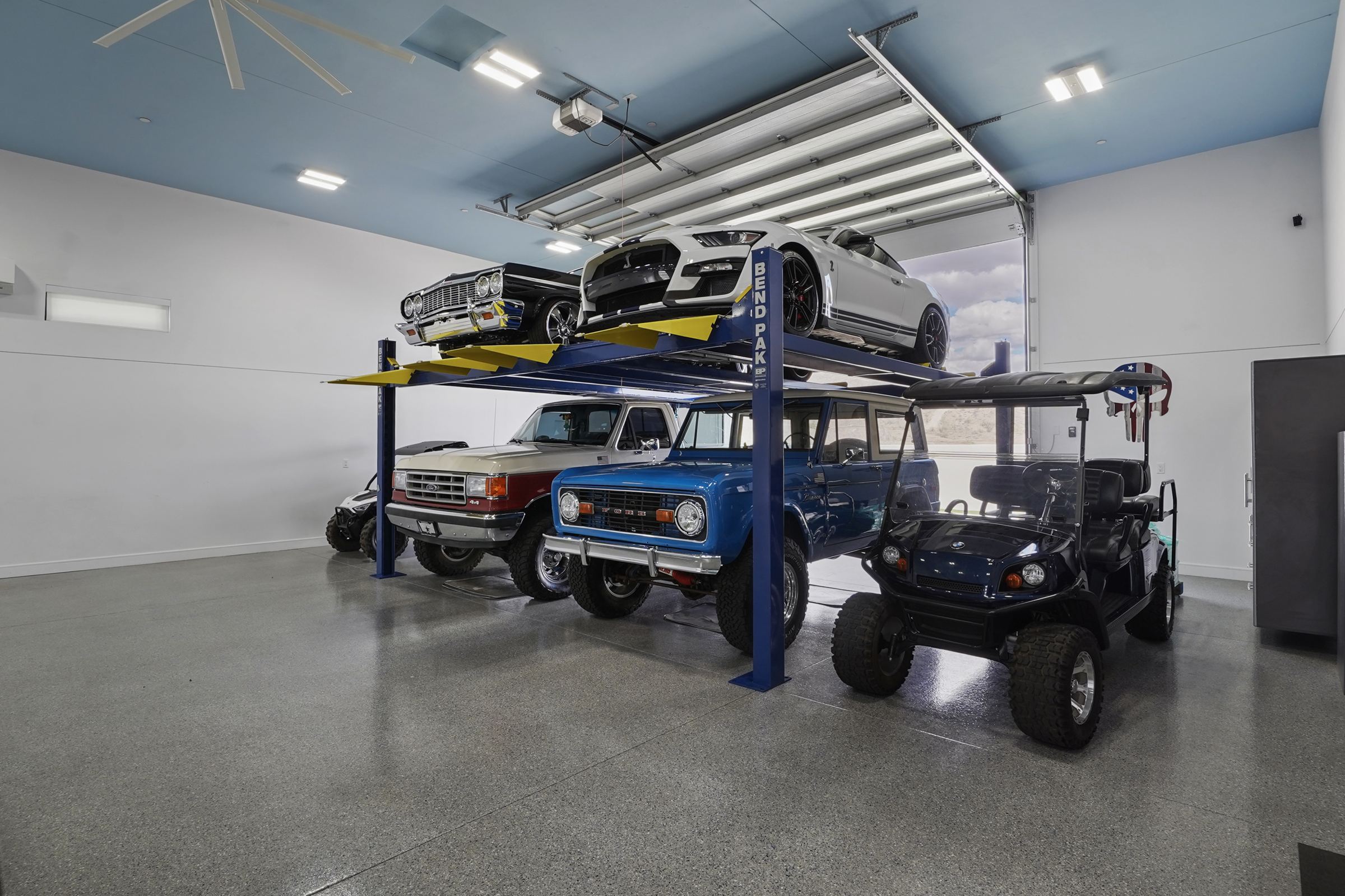 Broncos stacked on a car lift above side-by-sides in the garage at 6269 Avienda De Las Colinas